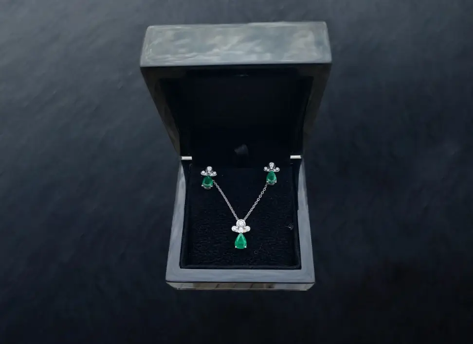Emerald and diamond earrings with matching pendant displayed in a luxury box — example of a bespoke jewellery gift created through Design in a Box.